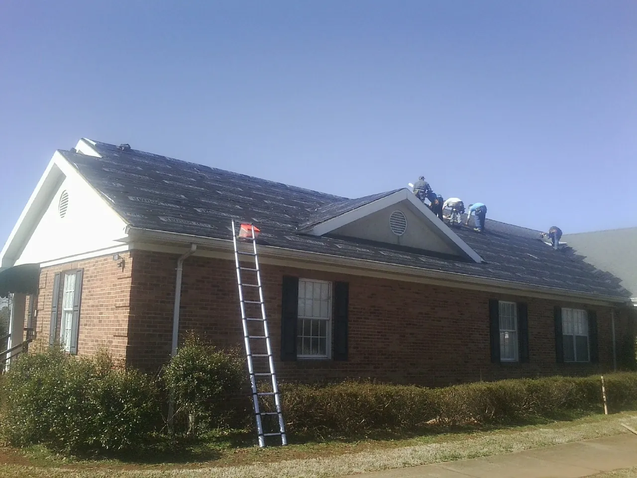 Crew tearing shingles off a brick ranch roof with a ladder set — Emergency Roof Repair work by our crew in Lake Harmony