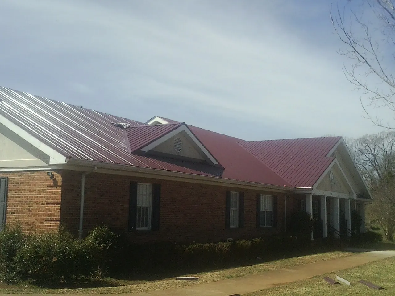 Red metal roof with gabled entries on a long brick building, from a Hail Damage Roof Repair job in Lake Harmony