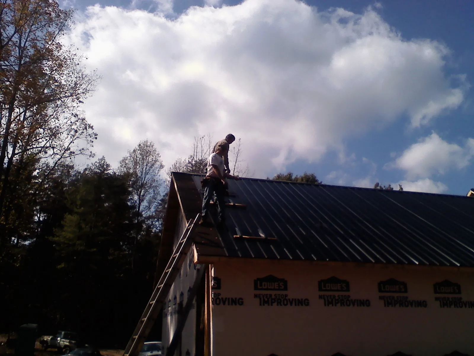 Roofer fastening dark metal panels high against a cloudy sky, from a Roof Inspection job in Lake Harmony