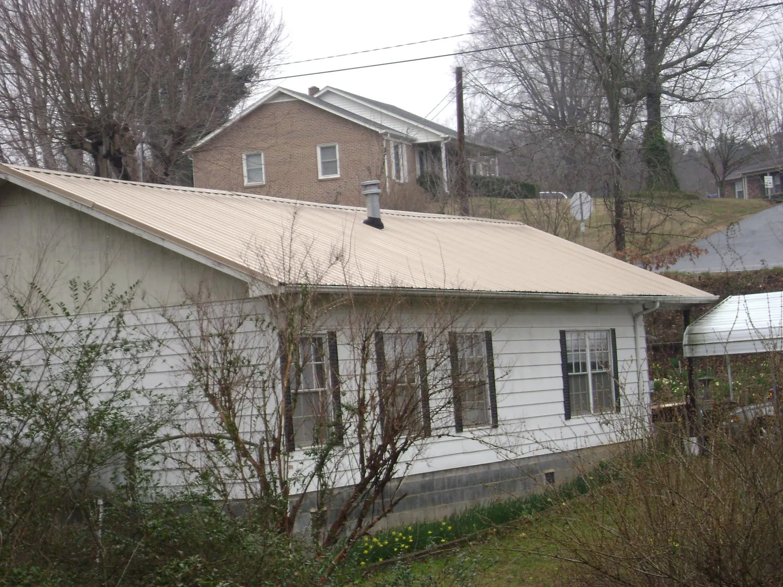 Tan metal roof on a white sided house set into a hillside — Commercial Roofing by Roofing Brothers in Lake Harmony