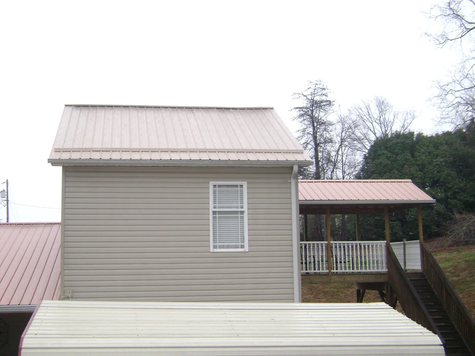 Tan metal roofs on a two story addition and attached porch, from a Roof Replacement job in Lake Harmony